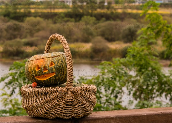 Jack-O-Lantern in wicker basket sitting on wooden railing with river and trees blurred out in background in South Korea