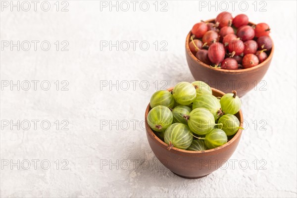 Fresh red and green gooseberry in clay bowl on gray concrete background. side view, copy space
