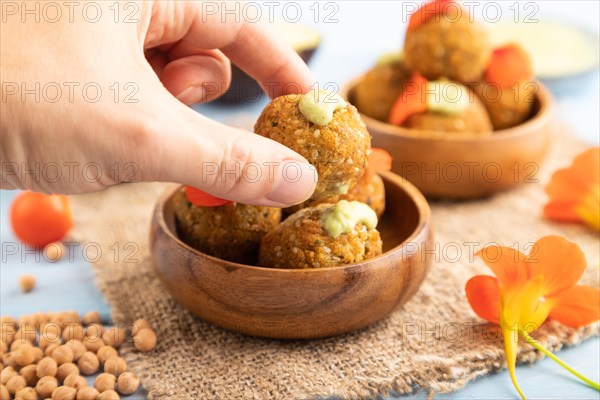 Falafel with guacamole on blue wooden background and linen textile with hand. Side view, close up, selective focus
