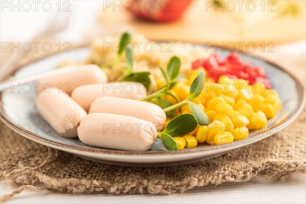 Mixed quinoa porridge, sweet corn, pomegranate seeds and small sausages on white wooden background. Side view, close up, selective focus. Food for children, healthy food concept