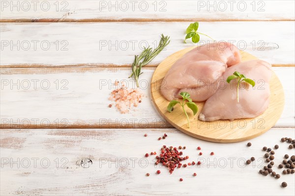 Raw chicken breast with herbs and spices on a wooden cutting board on a white wooden background. Side view, copy space