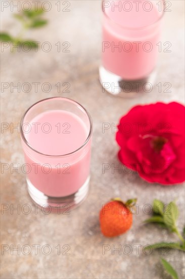 Sweet strawberry liqueur in glass on a gray concrete background and orange textile. side view, close up, selective focus