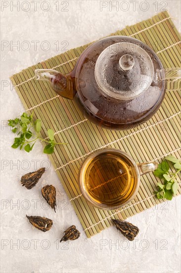 Red tea with herbs in glass on gray concrete background and linen textile. Healthy drink concept. Top view, flat lay
