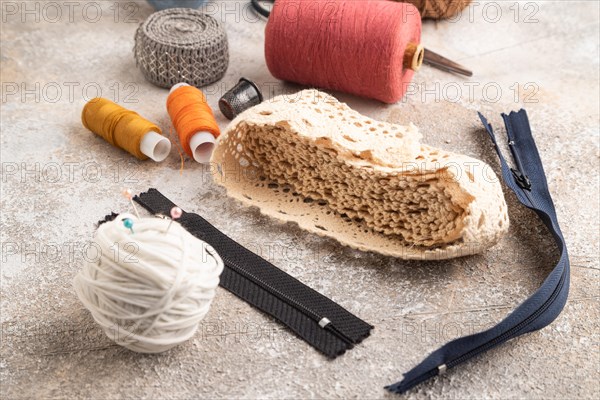 Sewing accessories: scissors, thread, thimbles, braid on brown concrete background. Side view, close up