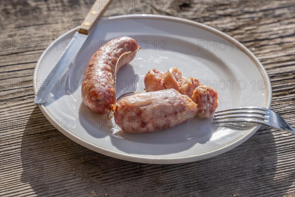 A Plate with Luganighe Sausage with Fork and Knife on a Wood Table with Sunlight in Lugano, Ticino, Switzerland, Europe