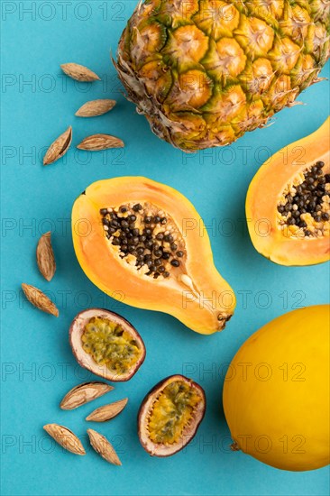 Ripe cut papaya, pineapple, melon, passion fruit, almonds on blue pastel background. Top view, flat lay, close up. Tropical, healthy food, vacation, holidays concept