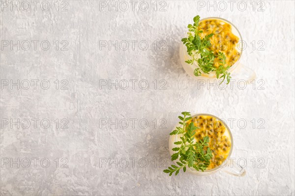 Yogurt with passionfruit and marigold microgreen in glass on gray concrete background. Top view, flat lay, copy space