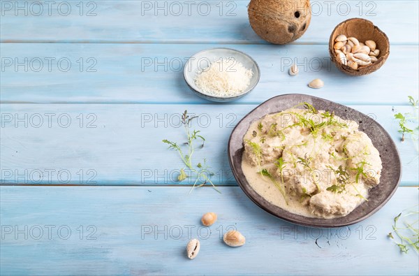 Stewed chicken fillets with coconut milk sauce and mizuna cabbage microgreen on blue wooden background. side view, copy space