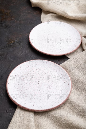 Two empty white plates on black concrete background and linen textile. Side view, close up