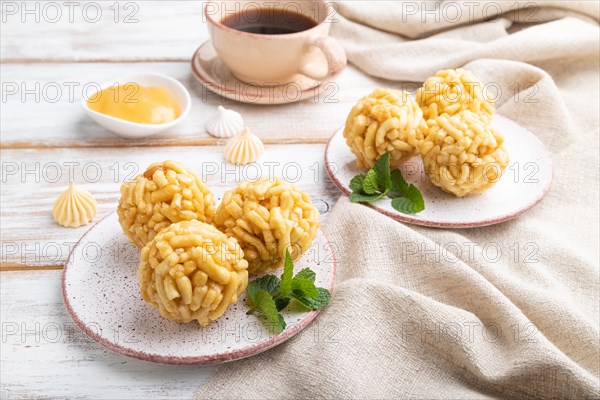 Traditional Tatar candy chak-chak made of dough and honey with cup of coffee on a white wooden background and linen textile. Side view, close up