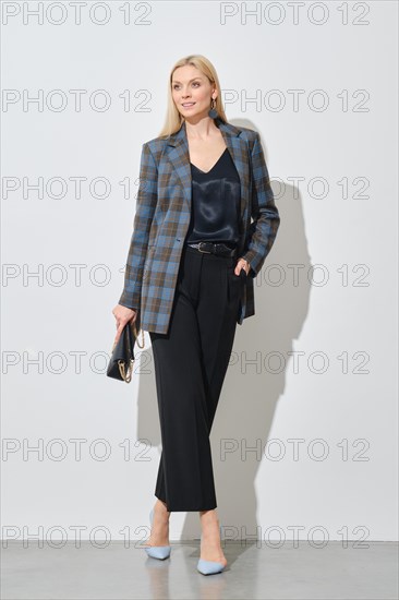 Modern businesswoman in stylish checkered jacket and loose trousers holding handbag