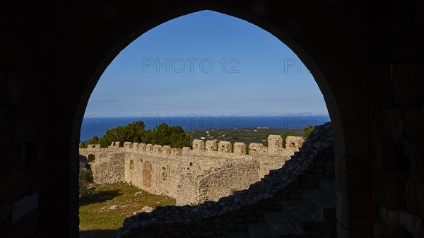 View through a stone arch onto historic fortress walls with blue sky and sea in the background, Chlemoutsi, High Medieval Crusader Castle, Kyllini Peninsula, Peloponnese, Greece, Europe