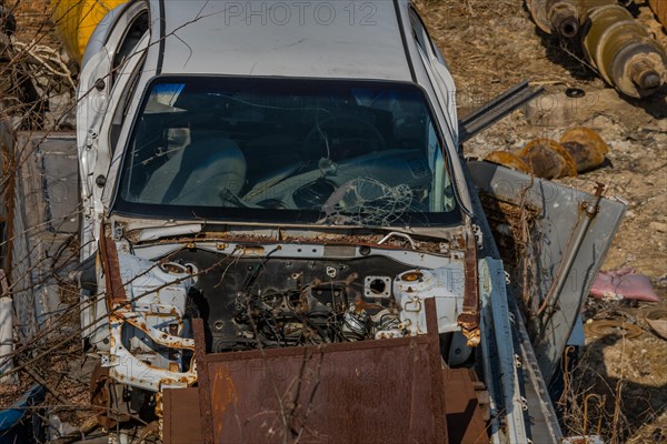 Crashed automobile with engine and hood removed sitting in junkyard on sunny day