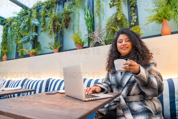 Portrait with copy space of a smiling woman drinking coffee while using laptop in a cafeteria