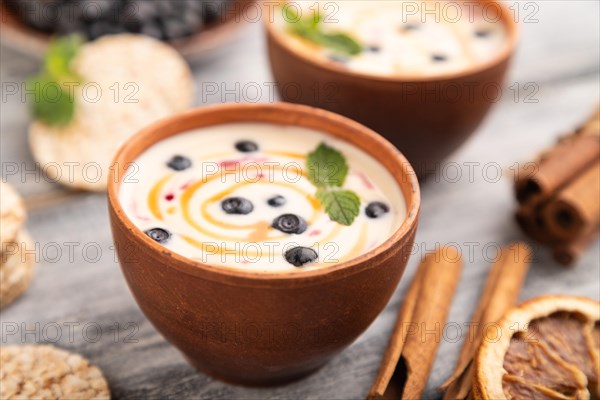 Yoghurt with bilberry and caramel in clay bowl on gray wooden background. side view, close up, selective focus