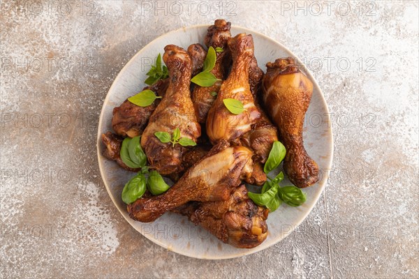 Smoked chicken legs with herbs and spices on a ceramic plate on a brown concrete background. Top view, flat lay, close up