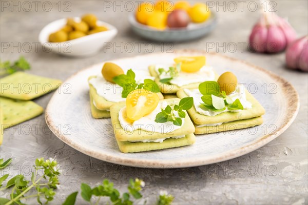 Green cracker sandwiches with cream cheese and cherry tomatoes on gray concrete background. side view, close up, selective focus