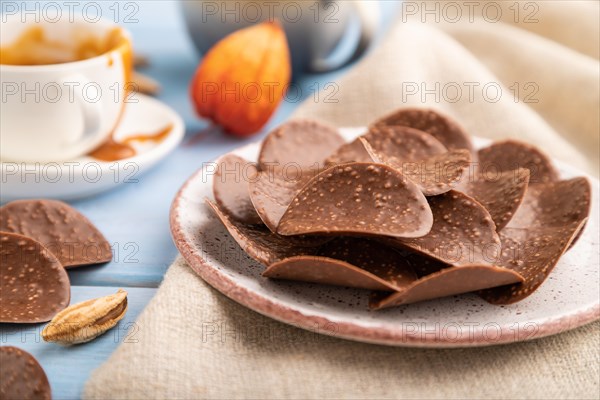 Chocolate chips with cup of coffee and caramel on a blue wooden background and linen textile. side view, close up, selective focus