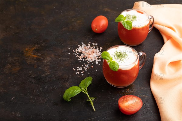 Tomato juice with basil, himalayan salt and sour cream in glass on a black concrete background with orange textile. Healthy drink concept. Side view, copy space