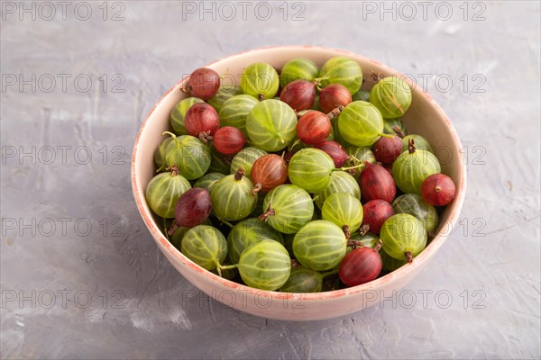 Fresh red and green gooseberry in ceramic bowl on gray concrete background. side view, close up