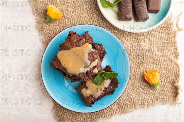 Chocolate brownie with caramel sauce with a cup of coffee on gray concrete background and linen textile. top view, flat lay, close up