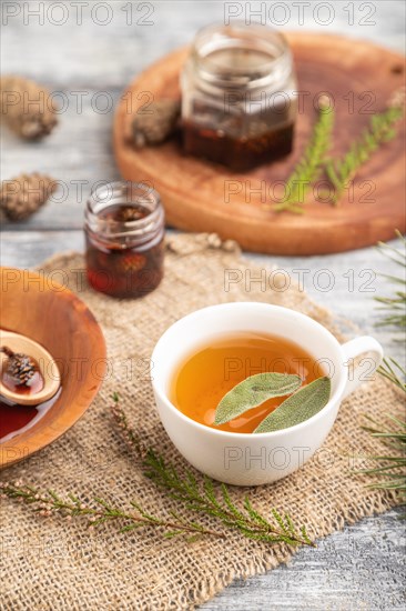 Pine cone jam with herbal tea on gray wooden background and linen textile. Side view, close up, selective focus