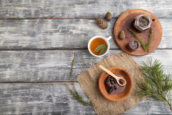 Pine cone jam with herbal tea on gray wooden background and linen textile. Top view, flat lay, copy space