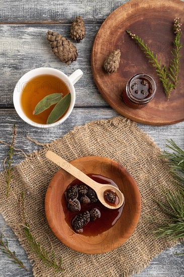 Pine cone jam with herbal tea on gray wooden background and linen textile. Top view, flat lay, close up