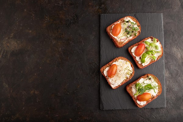 Red beet bread sandwiches with cream cheese, tomatoes and microgreen on black concrete background. top view, flat lay, copy space