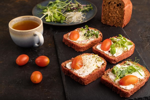 Red beet bread sandwiches with cream cheese, tomatoes and microgreen on black concrete background. Side view, close up