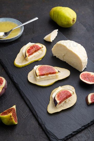 Summer appetizer with pear, cottage cheese, figs and honey on slate board on a black concrete background. Side view, close up