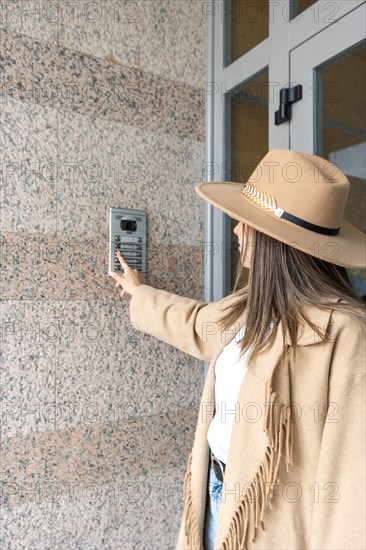 Vertical Side view of unrecognizable woman wearing a hat pushing the button of the intercom of building