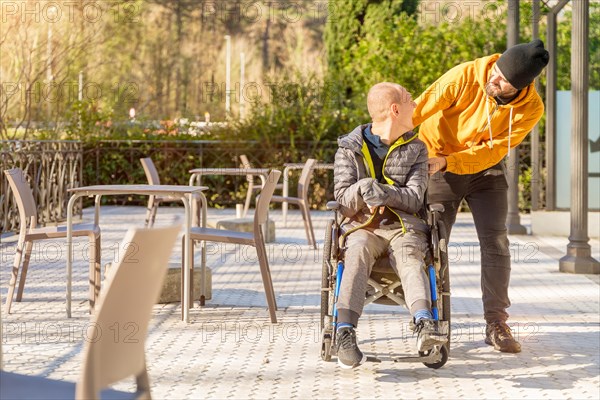 Photo with copy space of a happy disabled man and friend talking while walking along an urban park