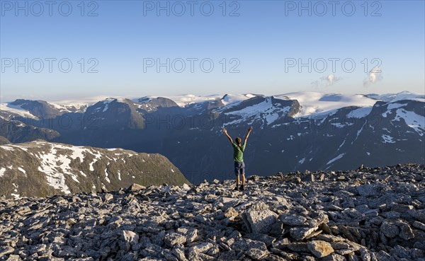 Mountain panorama with mountain peaks and Jostedalsbreen glacier, mountaineer stretches his arms in the air, at the summit of Skala, Loen, Norway, Europe