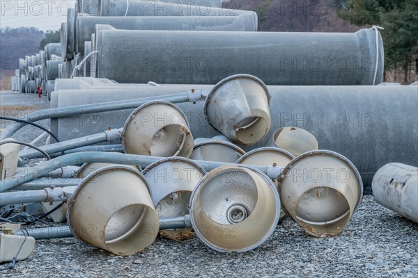 Old dirty street light fixtures laying on gravel in front of culverts at construction site