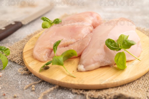 Raw chicken breast with herbs and spices on a wooden cutting board on a brown concrete background. Side view, close up, selective focus