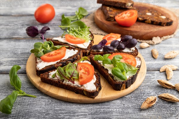 Grain rye bread sandwiches with cream cheese, tomatoes and microgreen on gray wooden background and linen textile. side view, close up