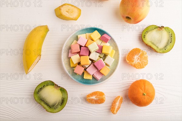 Various fruit jelly chewing candies on plate on white wooden background. apple, banana, tangerine, kiwi, top view, flat lay, close up