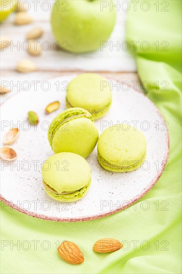 Green macarons or macaroons cakes with cup of coffee on a white wooden background and green linen textile. Side view, close up, selective focus