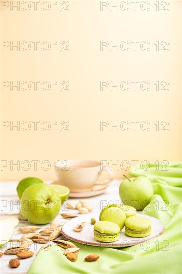 Green macarons or macaroons cakes with cup of coffee on a white and orange background and green linen textile. Side view, copy space, selective focus