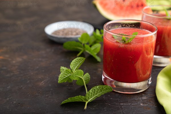 Watermelon juice with chia seeds and mint in glass on a black concrete background with green textile. Healthy drink concept. Side view, close up, selective focus