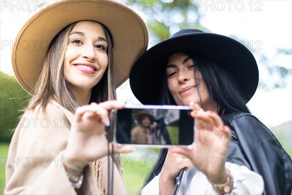 Front view of two stylish friends both grabbing a cell phones to take a selfie