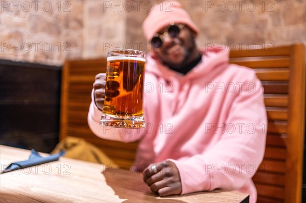 Cool african man toasting with a glass of beer sitting in a bar