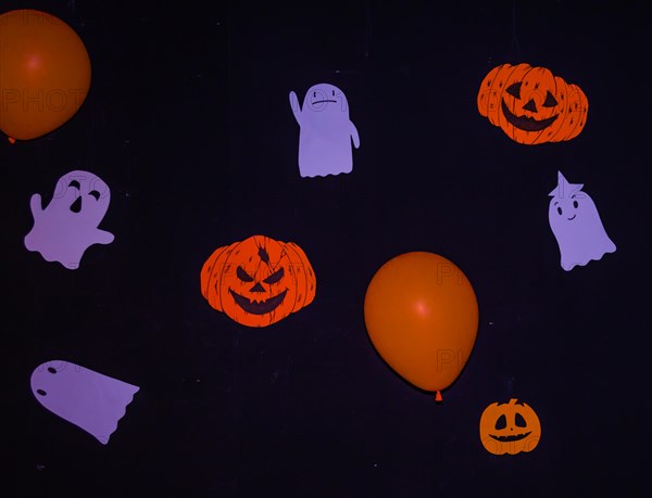 Halloween decorations of handmade ghosts, Jack-o-Lanterns, and orange balloons hanging on a black wall in South Korea