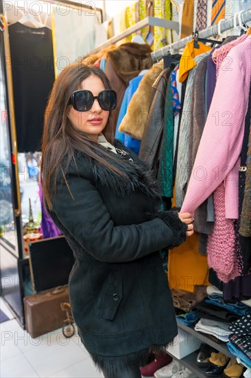 Vertical photo of a woman in sunglasses and jacket shopping in a fashion store