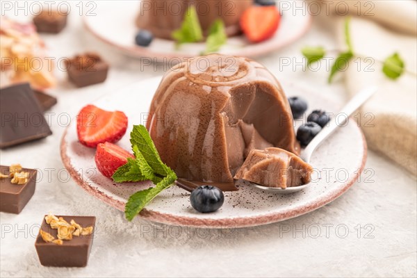 Chocolate jelly with strawberry and blueberry sliced with spoon on gray concrete background and linen textile. side view, close up, selective focus