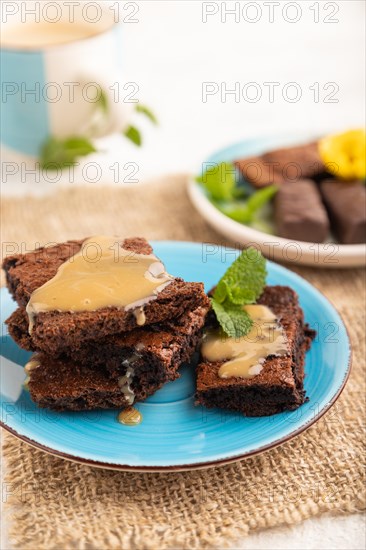 Chocolate brownie with caramel sauce with a cup of coffee on gray concrete background and linen textile. side view, close up, selective focus