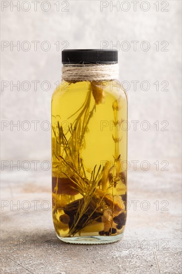 Sunflower oil in a glass jar with various herbs and spices, lavender, sesame, rosemary on a brown concrete background. Side view, close up