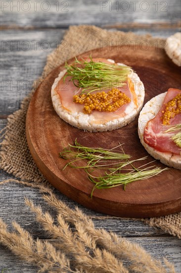 Puffed rice cake sandwiches with jerky salted meat, carrot microgreen on gray wooden background and linen textile. side view, close up, selective focus