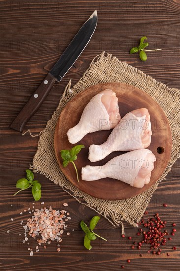 Raw chicken legs with herbs and spices on a wooden cutting board on a brown wooden background and linen textile. Top view, flat lay, close up
